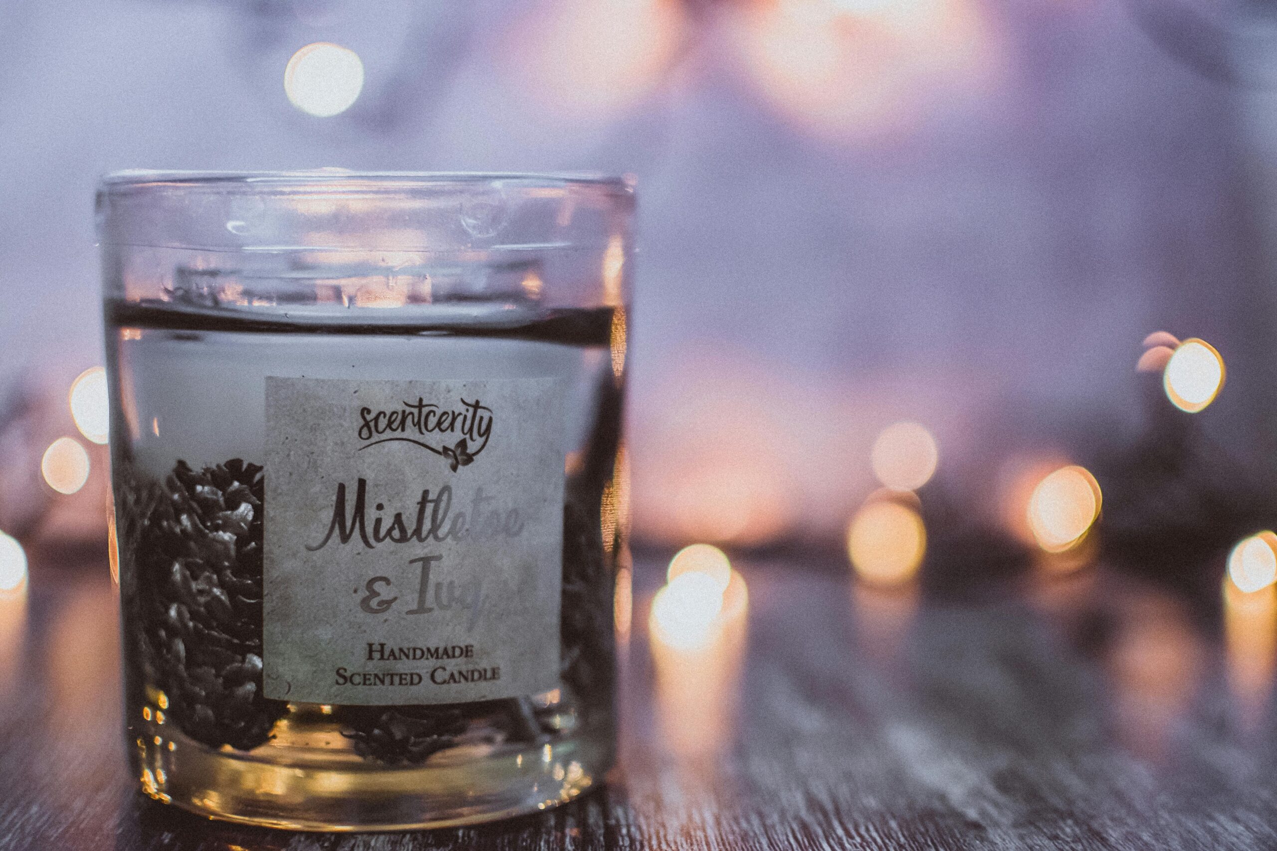 A close-up of a handmade mistletoe and ivy scented candle in a glass container with a soft bokeh background.