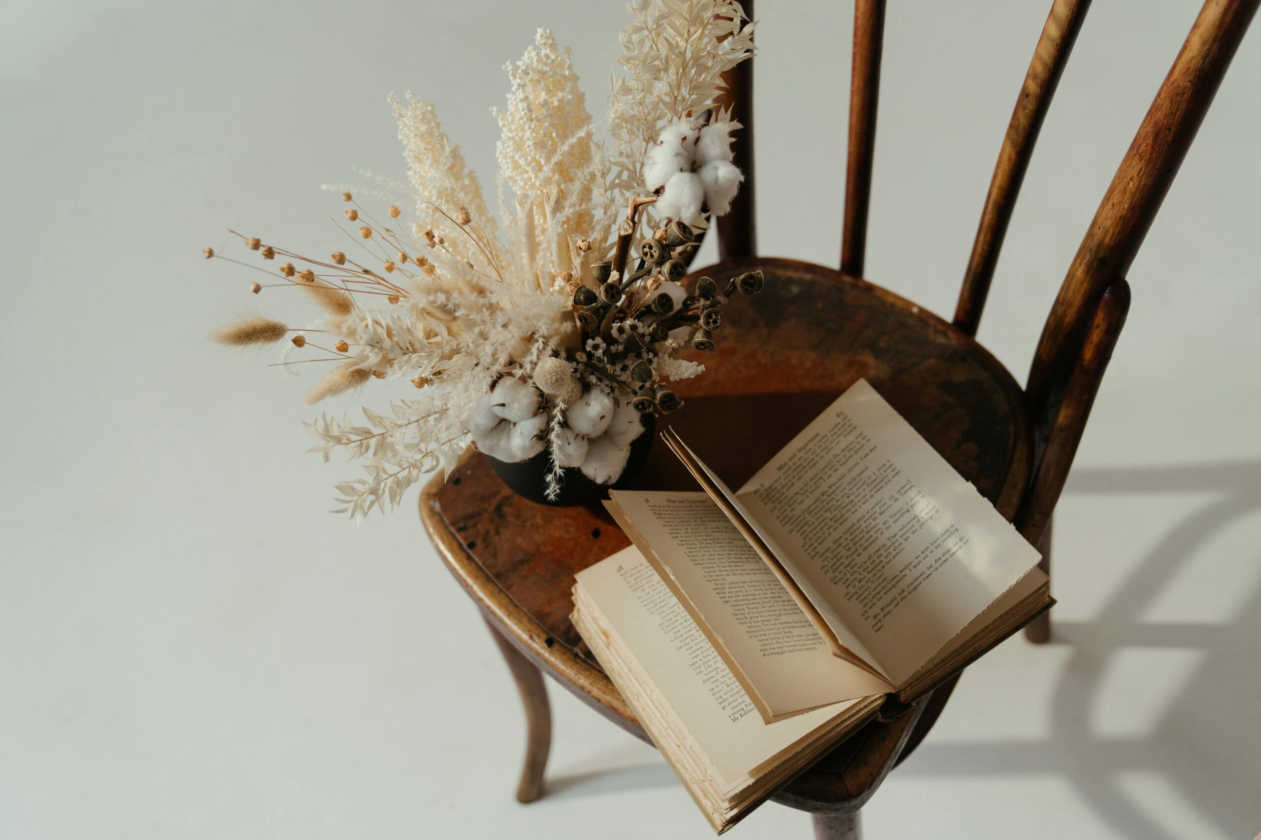 A dried flower bouquet and open book placed on a wooden chair, creating a rustic still life scene.