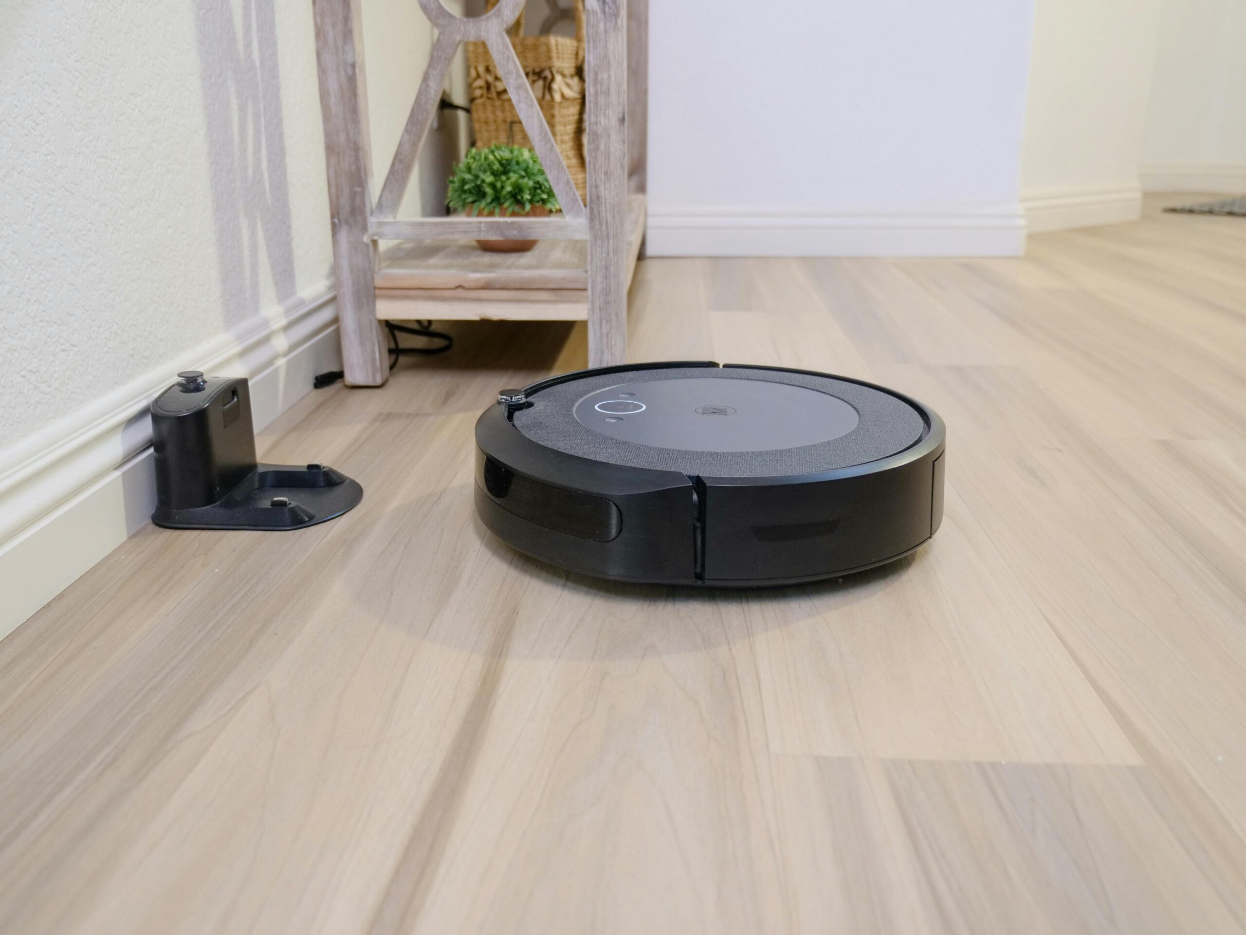 A sleek robotic vacuum navigates a clean hardwood floor beside a docking station.