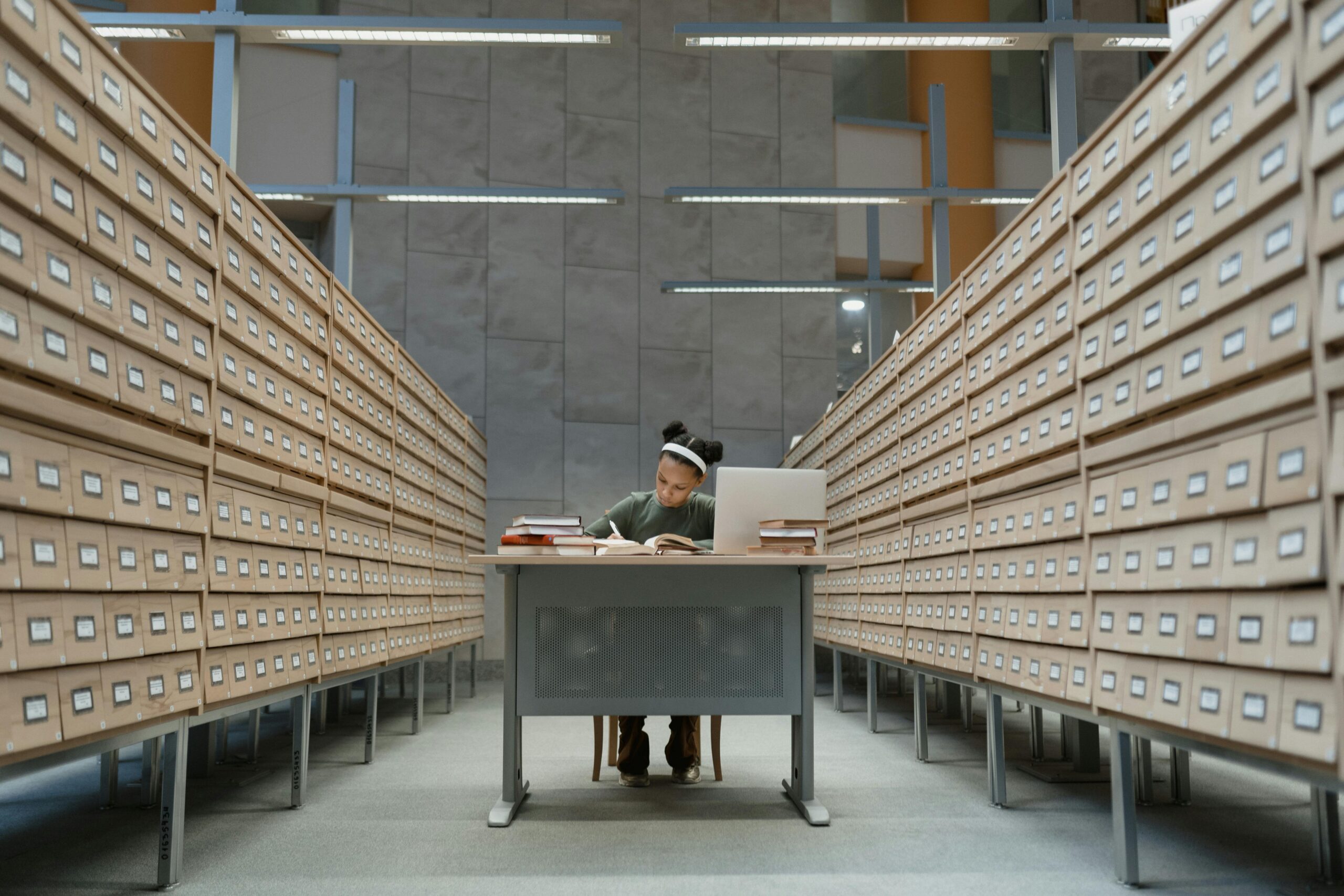 A student deeply focused on studying at a desk surrounded by library archive drawers.