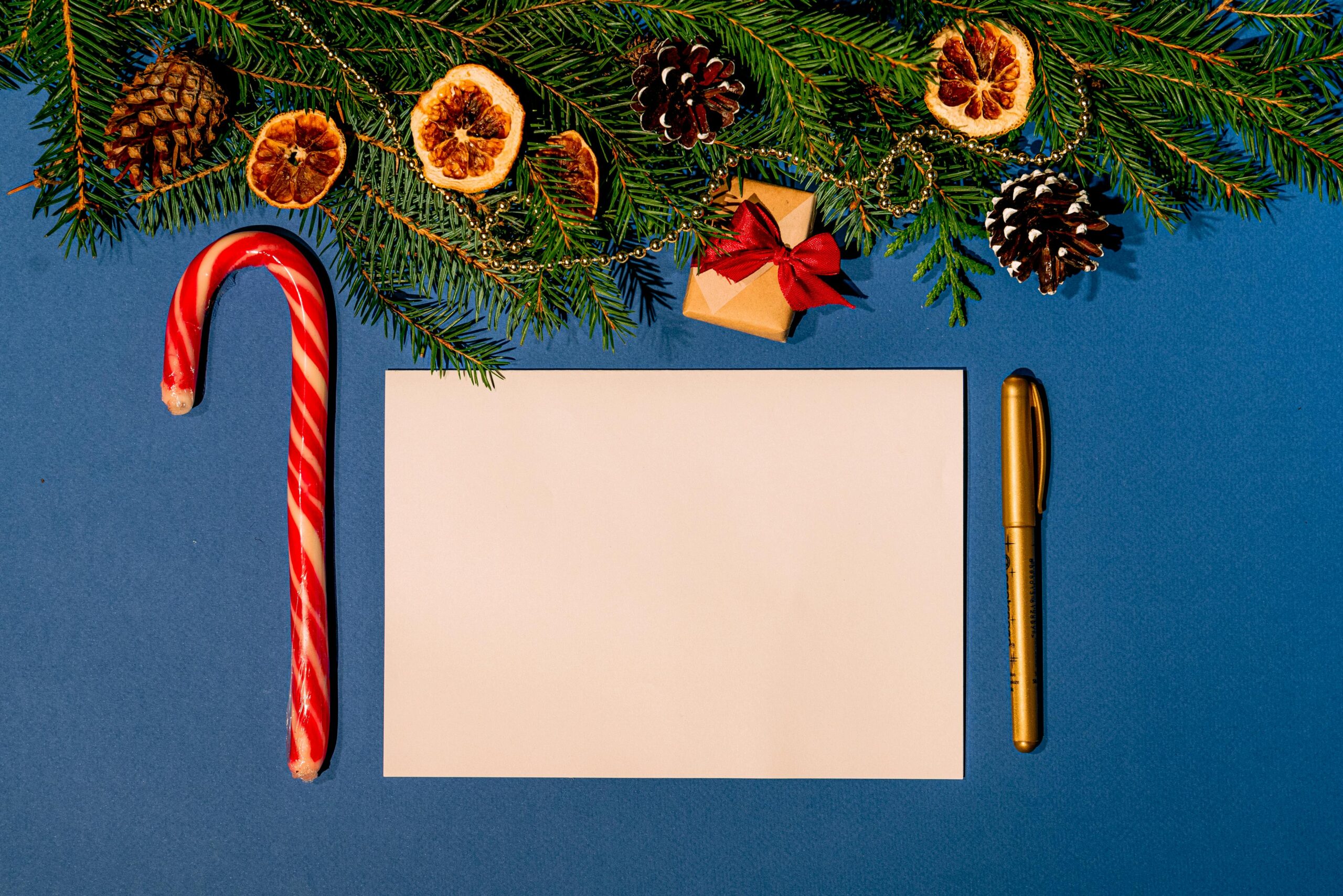 A top-down view of blank Christmas card surrounded by holiday decorations including a candy cane and pine cones.