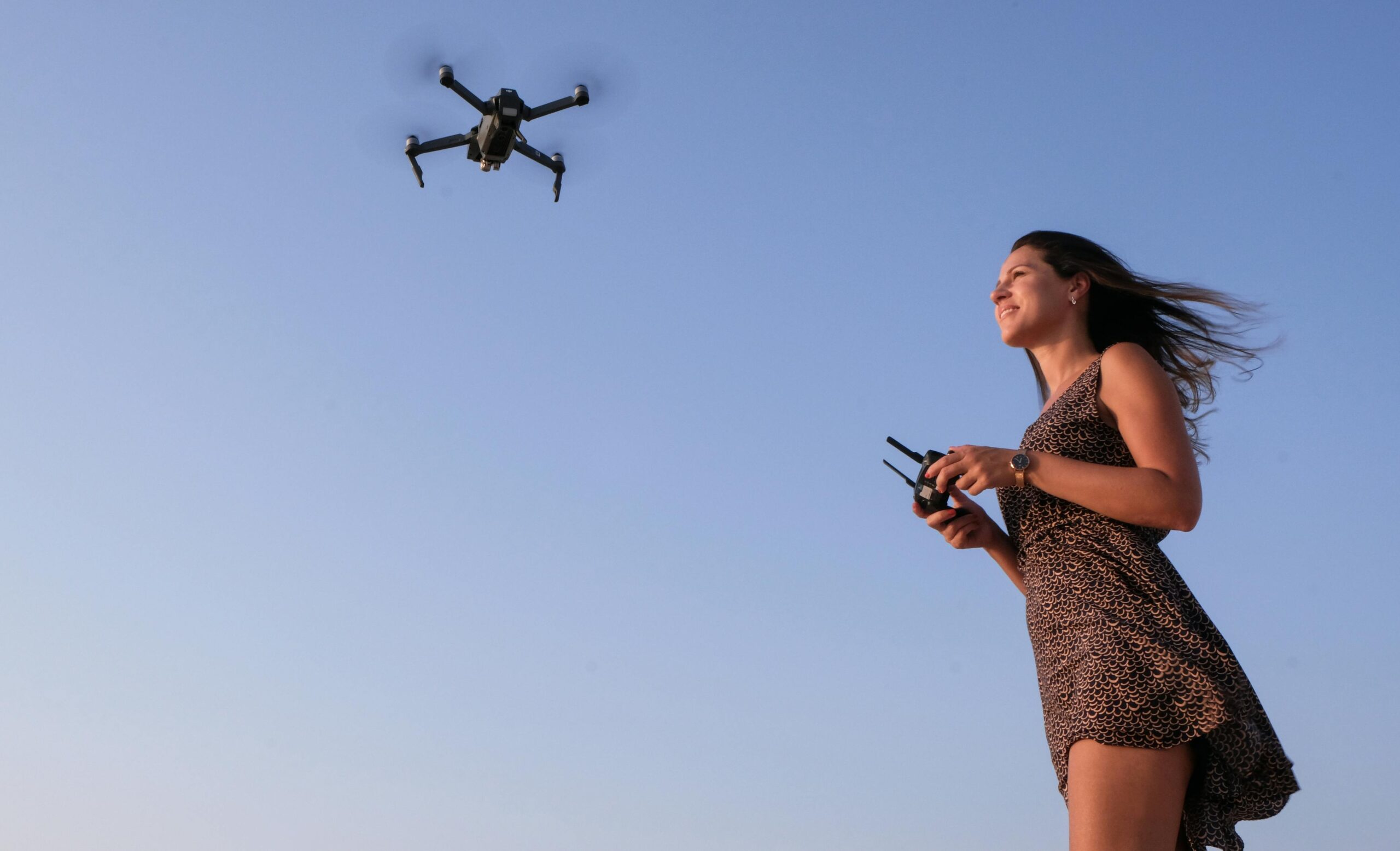 A woman enjoying flying a drone outdoors under a clear blue sky.