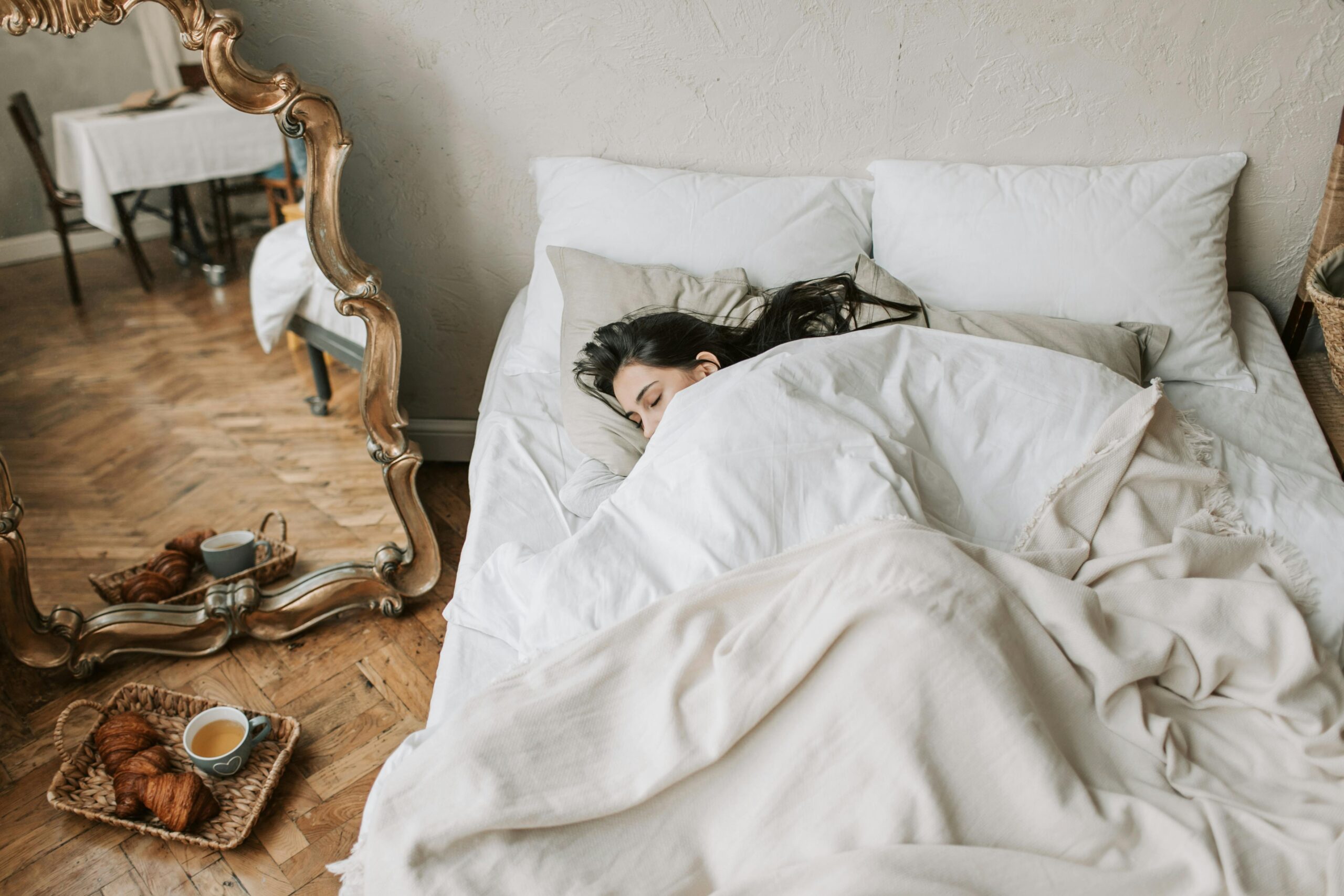 A woman peacefully sleeping in a cozy bed with croissants on the floor.