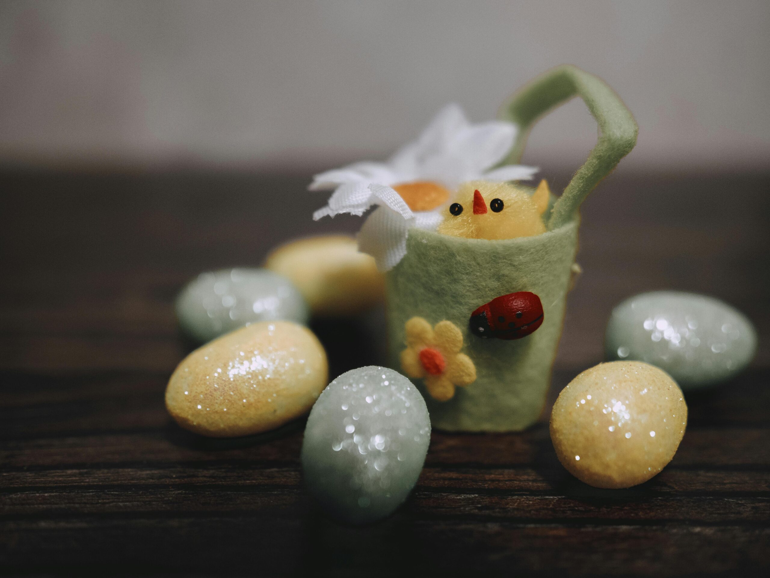 Charming Easter decoration with a felt basket, cute chick, and glittery eggs on a wooden table.