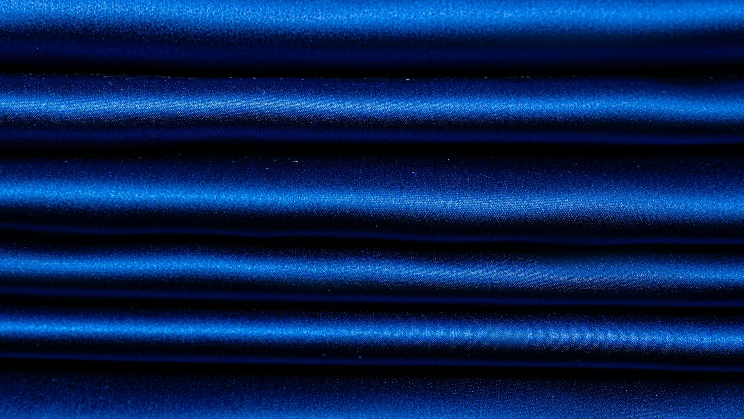 Close-up of luxurious blue silk fabric with smooth folds and rich texture for elegant backgrounds.