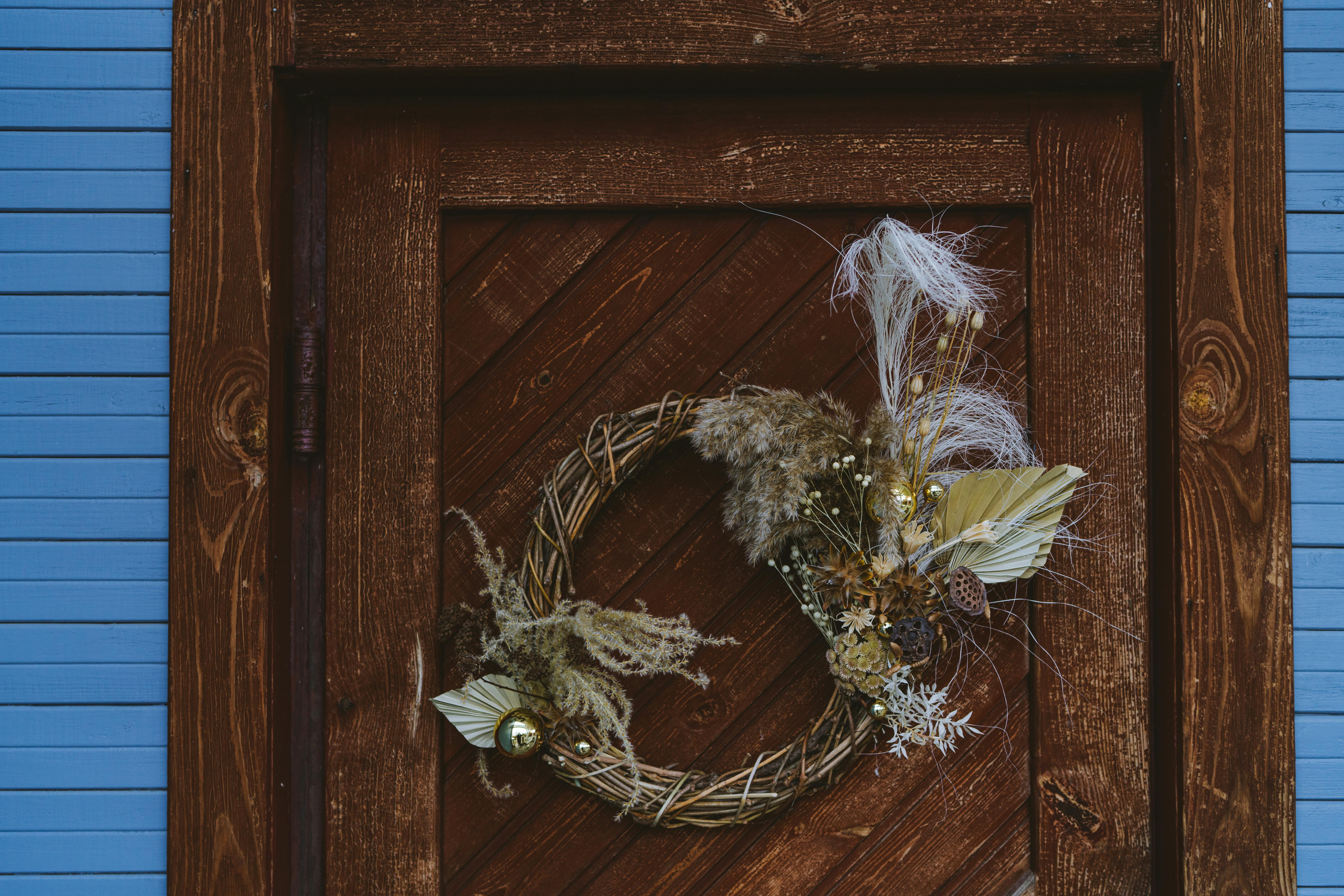 Decorative dried flower wreath on a rustic wooden door with blue siding, perfect for autumn decor.