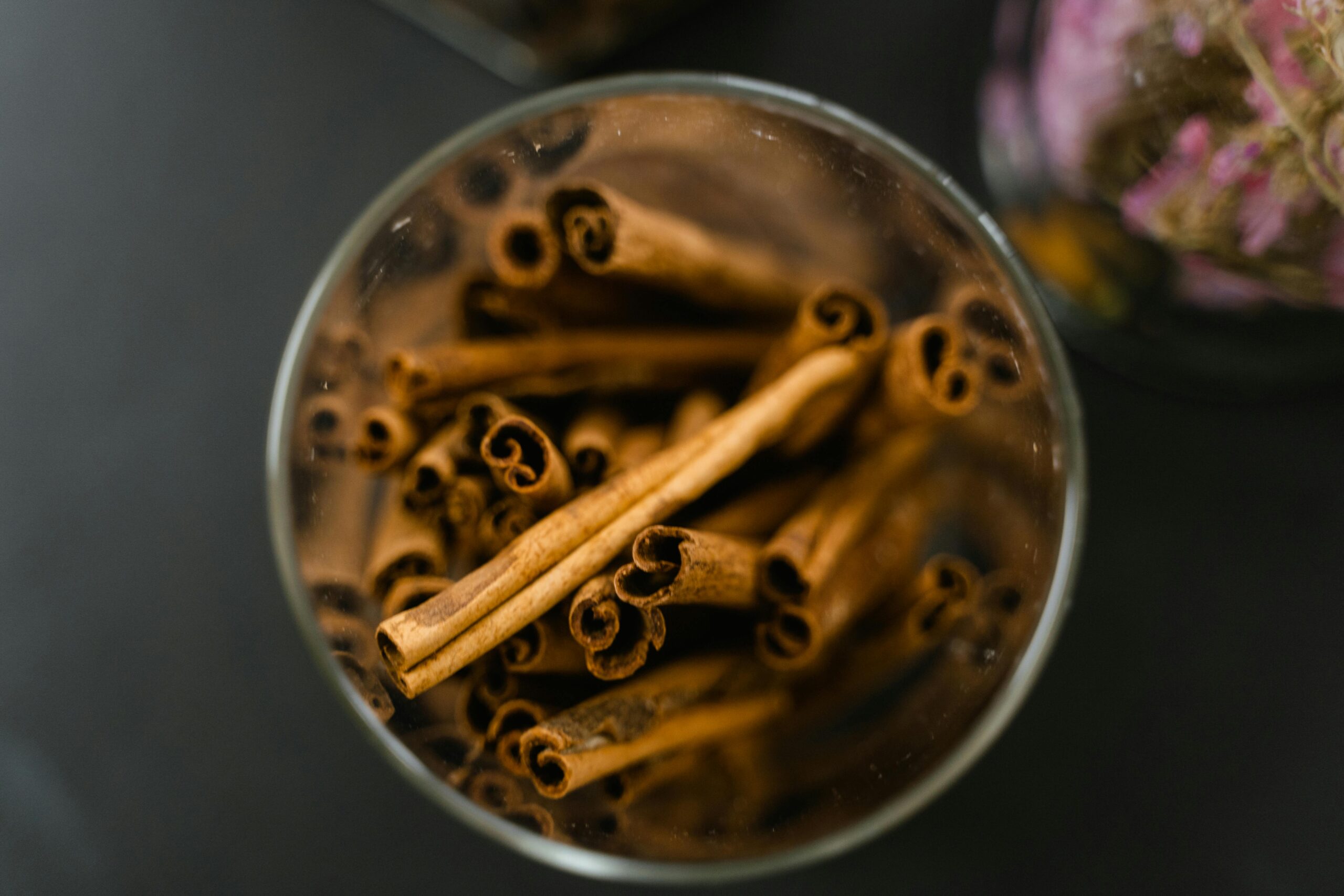 Aromatic cinnamon sticks in a glass jar on a black surface, offering a warm and inviting spice display.