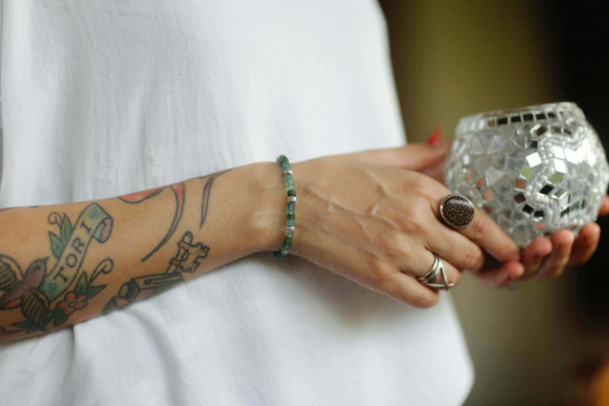 Крупный план декоративного мозайчного подсвечника в руках с татуировками.
