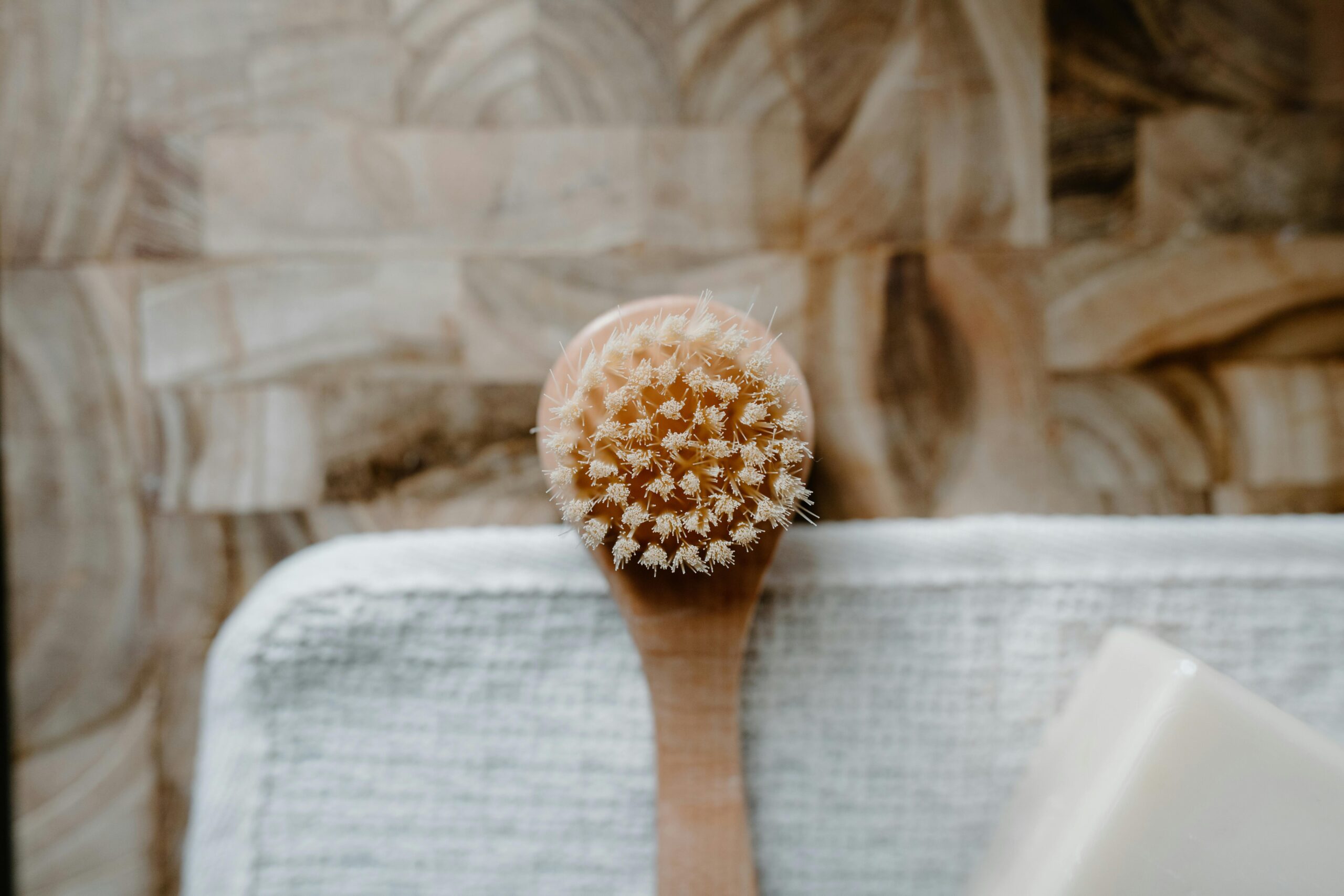 Close-up of a wooden body brush and soap on a towel, emphasizing self-care and hygiene.