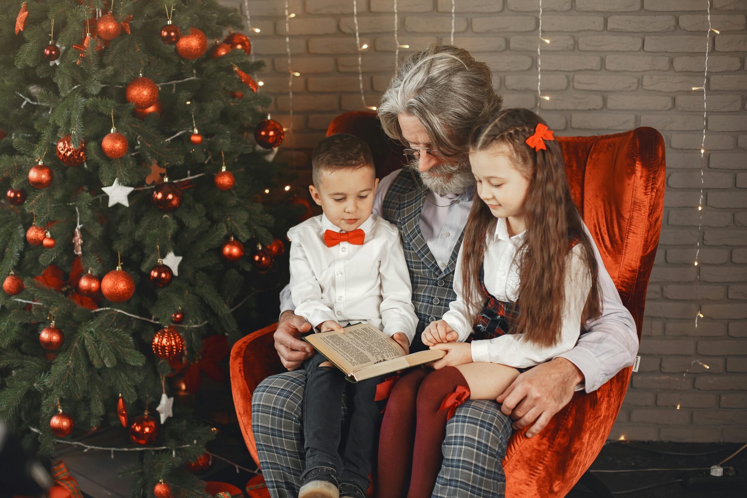 A warm family moment with a grandfather reading to kids by a decorated Christmas tree.