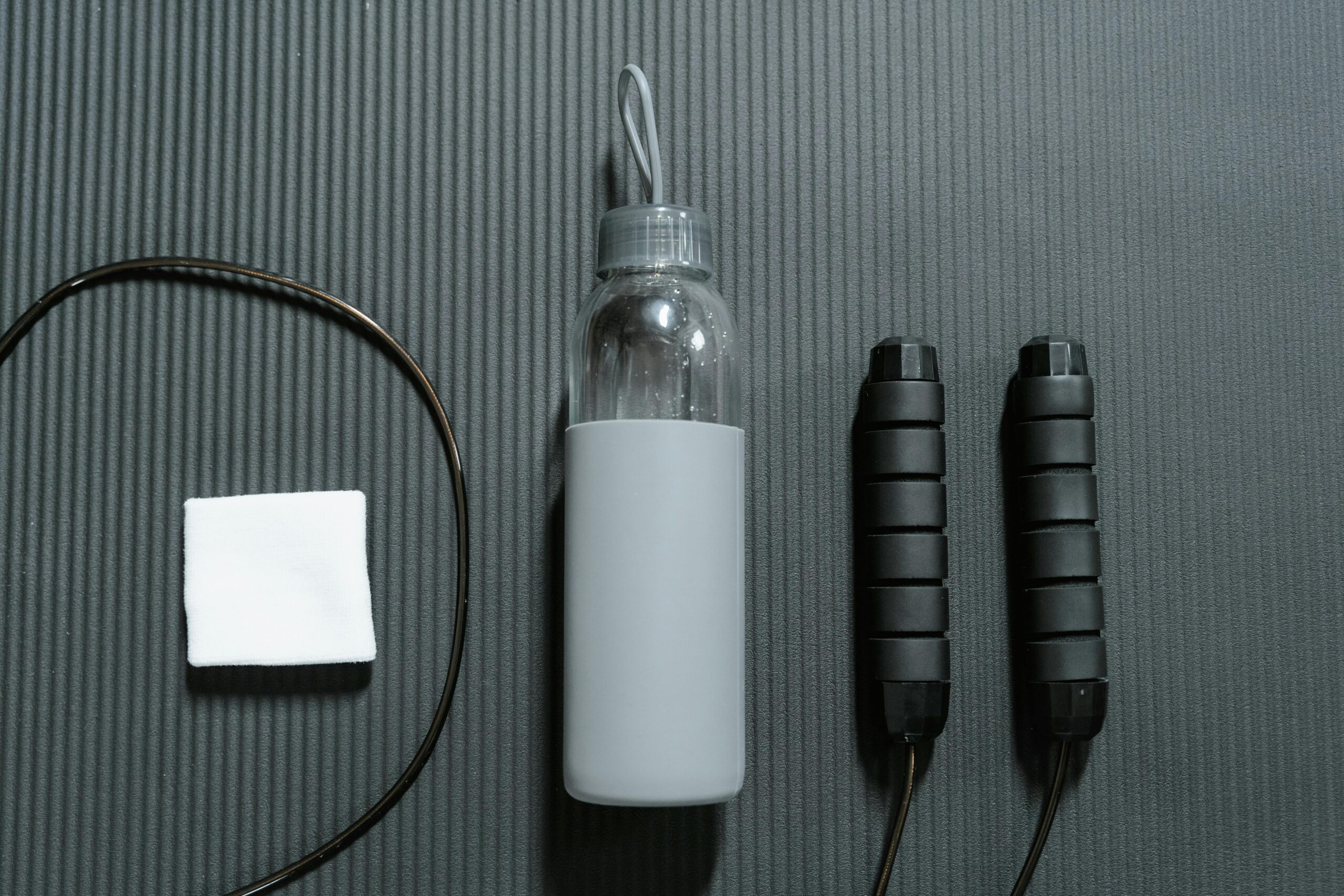 A neatly arranged flat lay of fitness gear including a water bottle and jump rope on a yoga mat.