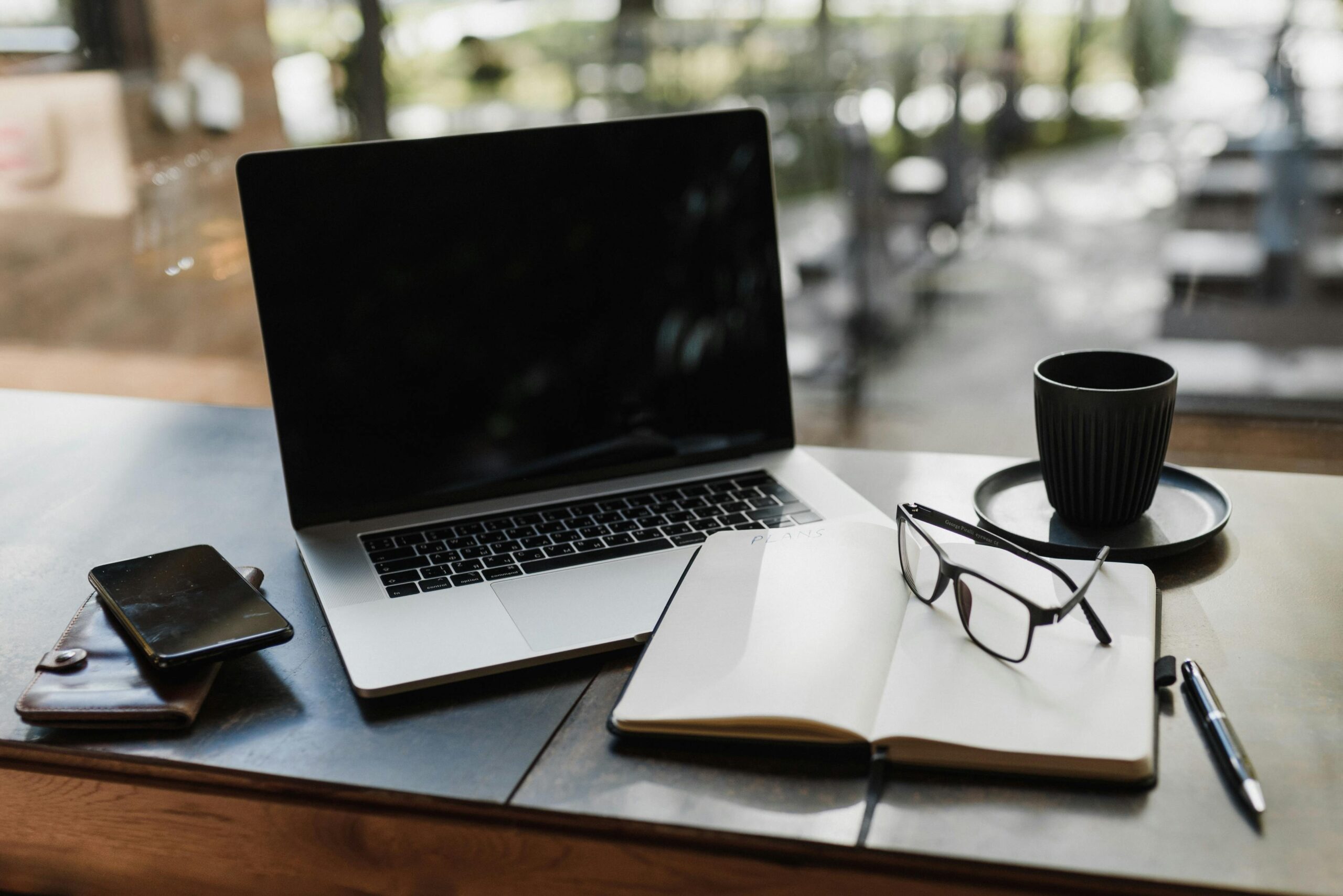 Workspace setup featuring a laptop, notepad, glasses, and coffee cup for productivity.
