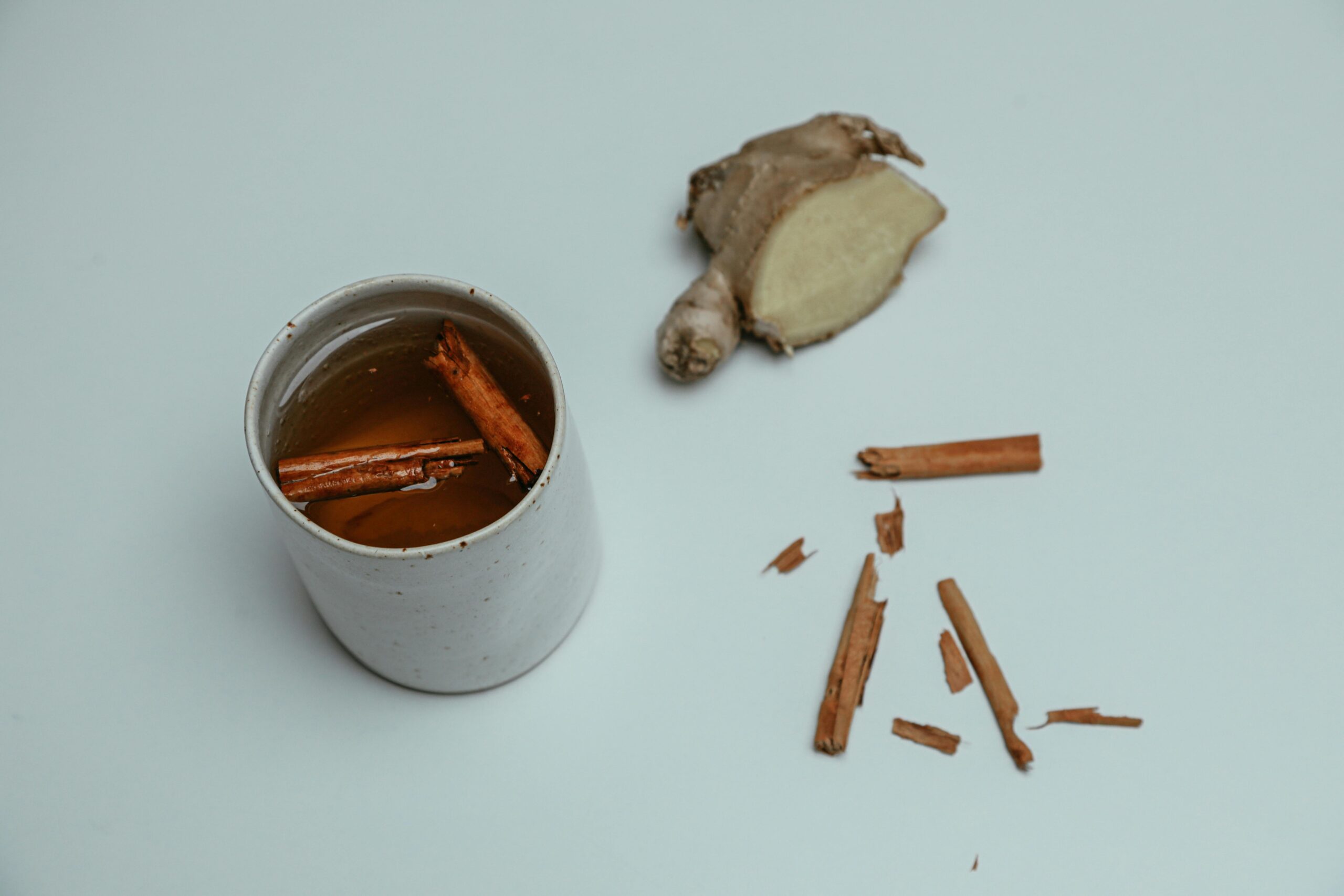 A cup of tea infused with cinnamon sticks and ginger on a white background.