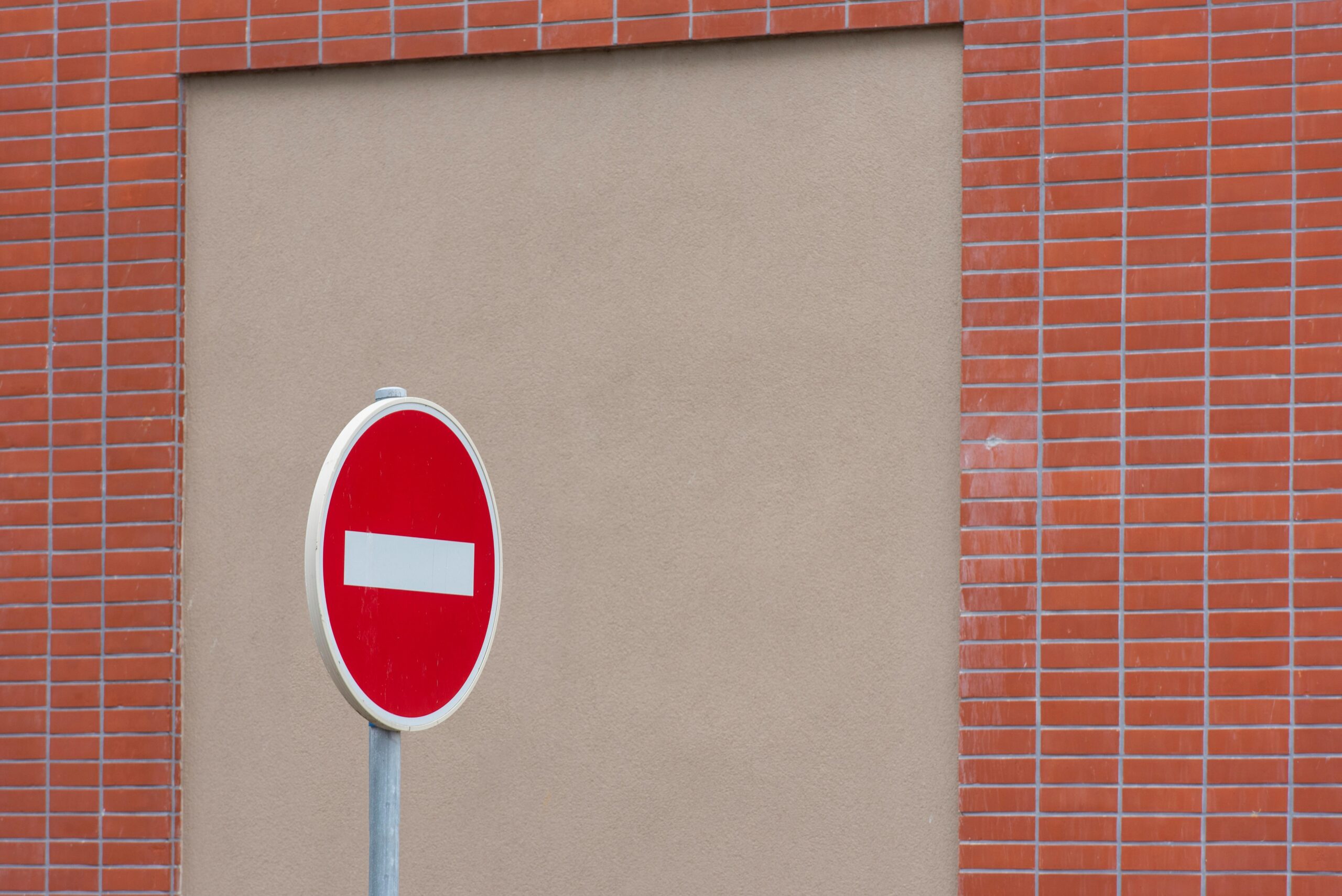 A red no entry traffic sign stands in front of a brick wall.