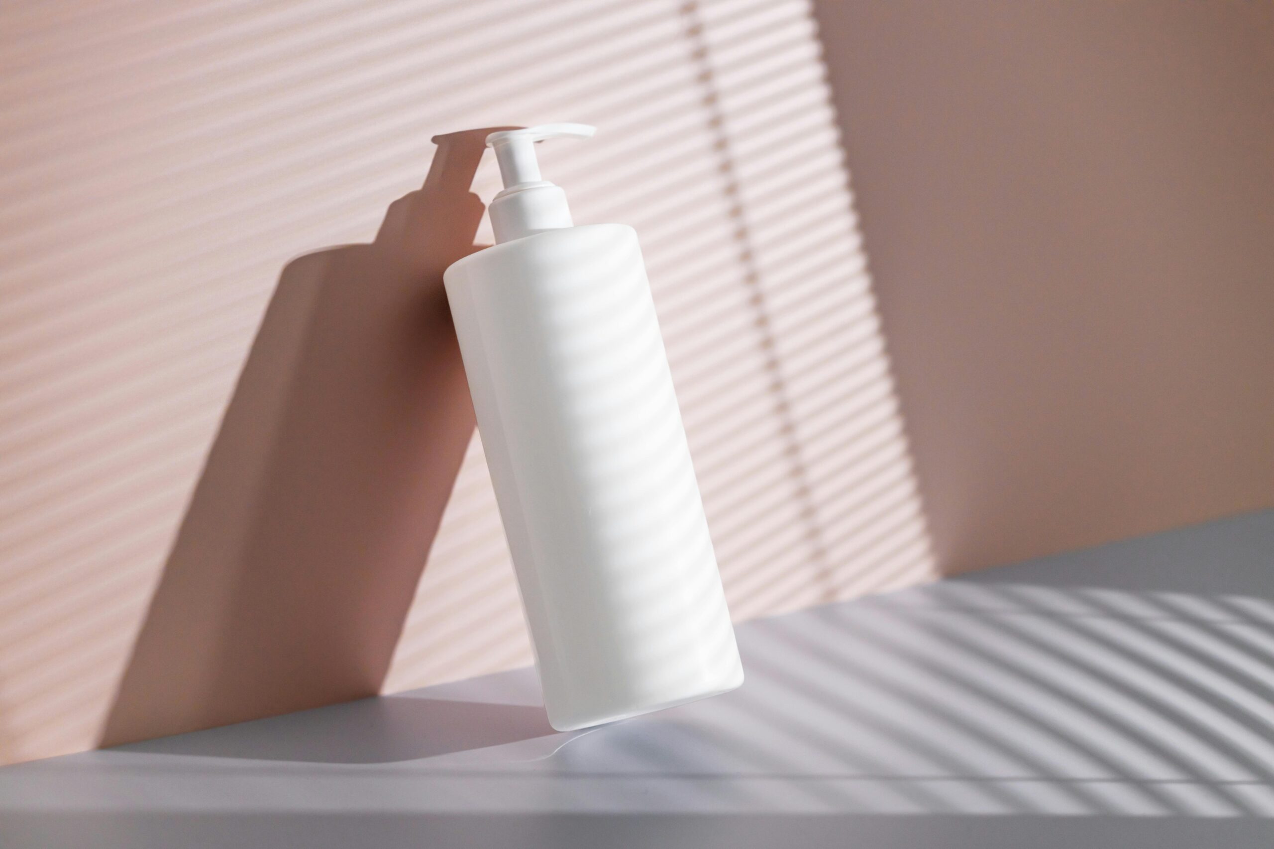 White pump bottle casting shadow in sunlight with pink background, ideal for cosmetic branding.