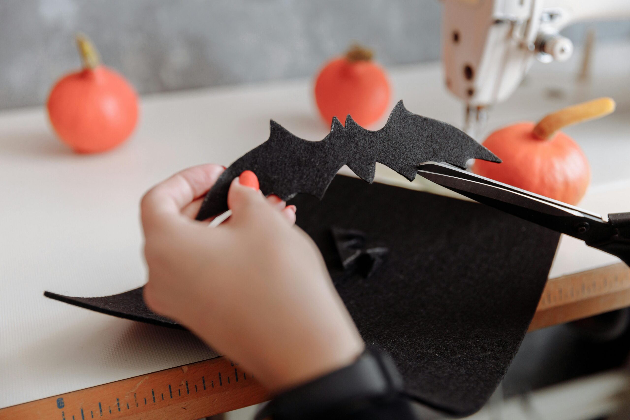 Close-up of hands cutting a black felt bat for Halloween crafts with pumpkins in the background.