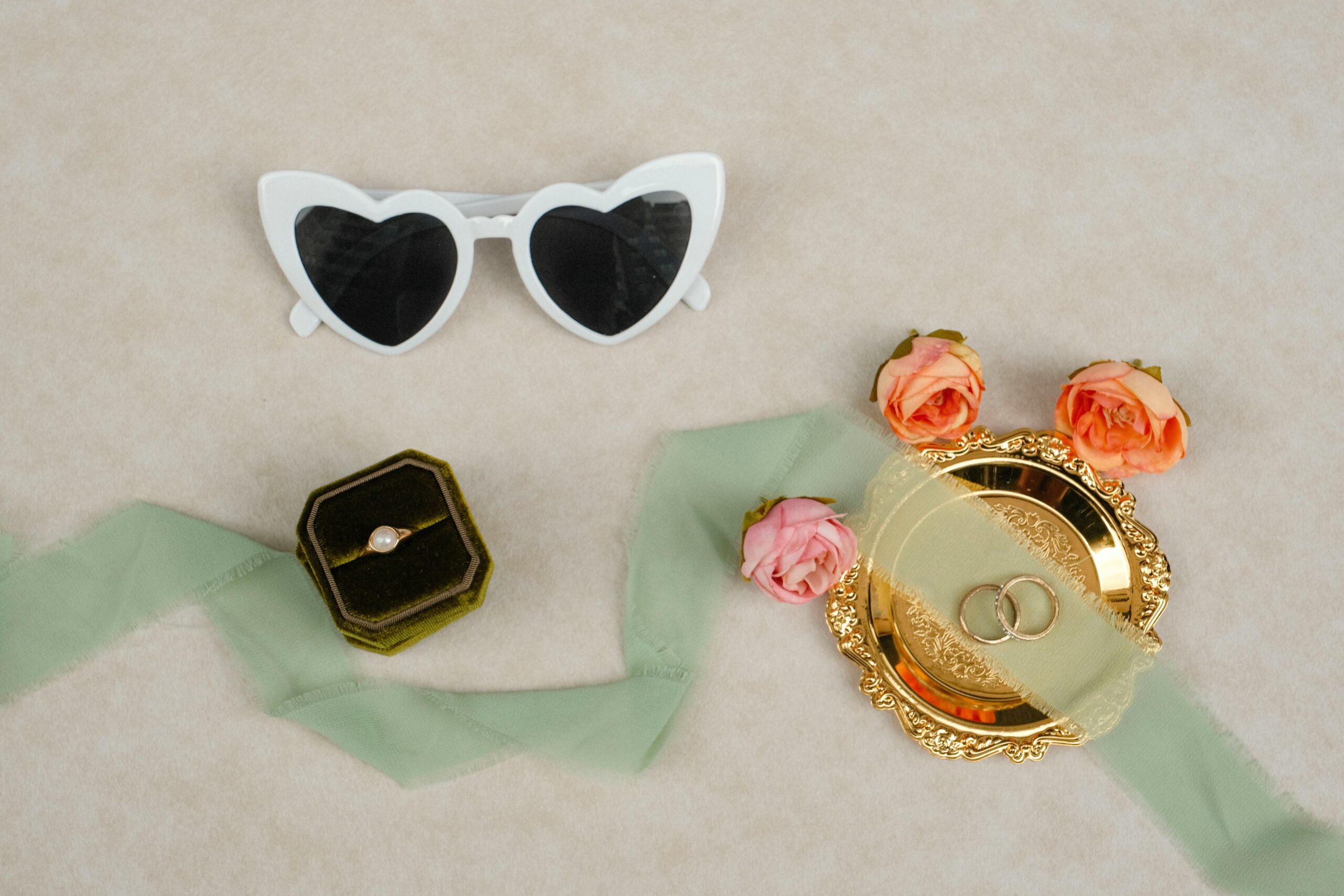 Stylish wedding accessories including heart sunglasses, rings, and roses on a light background.