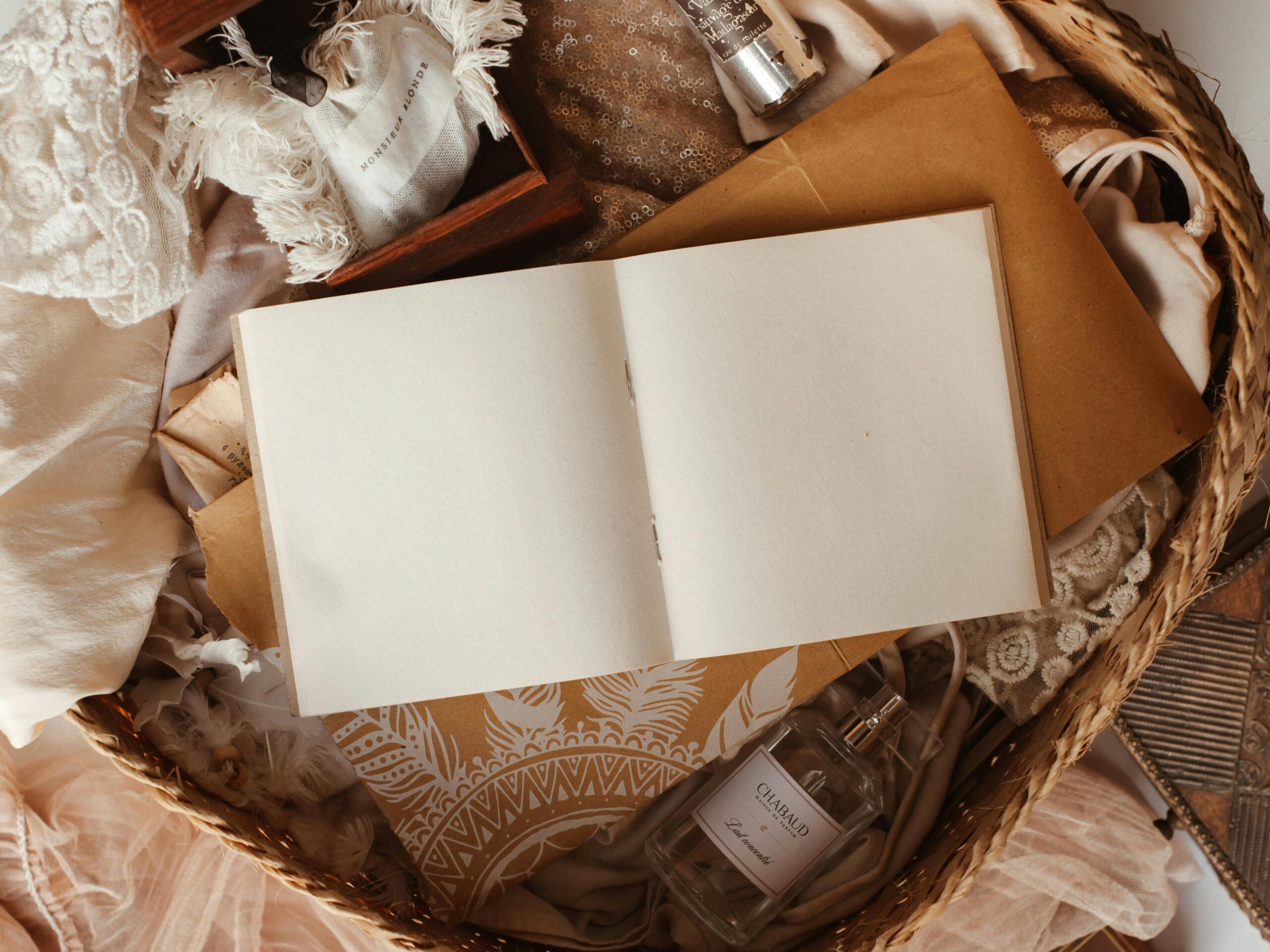 A flat lay image of an open notebook surrounded by various rustic and soft textured items in a basket.
