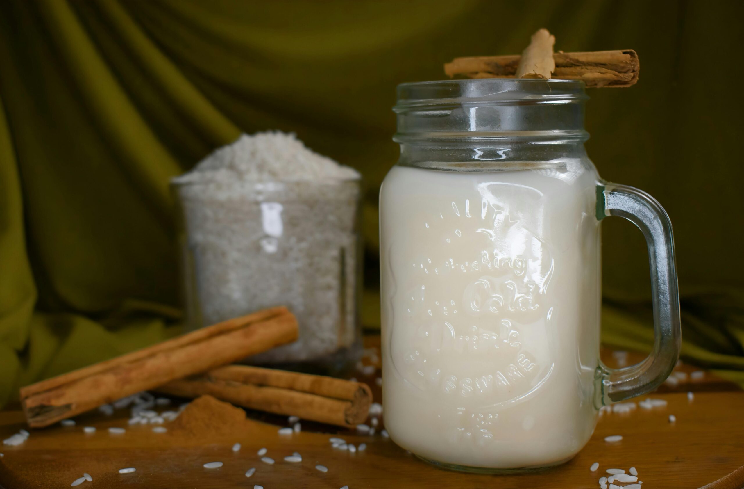 Glass jar of refreshing horchata garnished with cinnamon sticks and rice, creating a cozy homemade beverage scene.