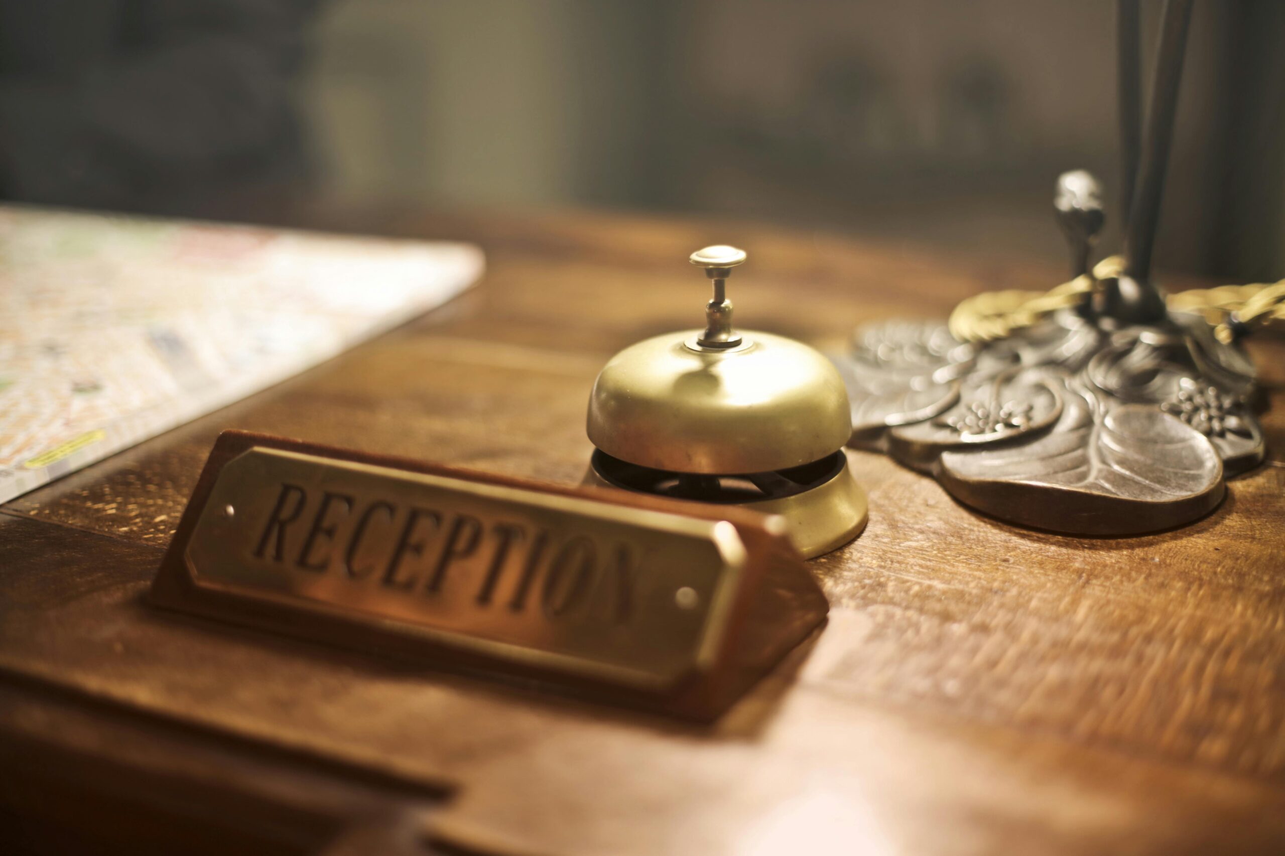 Old fashioned golden service bell and reception sign placed on wooden counter of hotel with retro interior. Регистрация гостей и автоматизация процессов в гостинице.