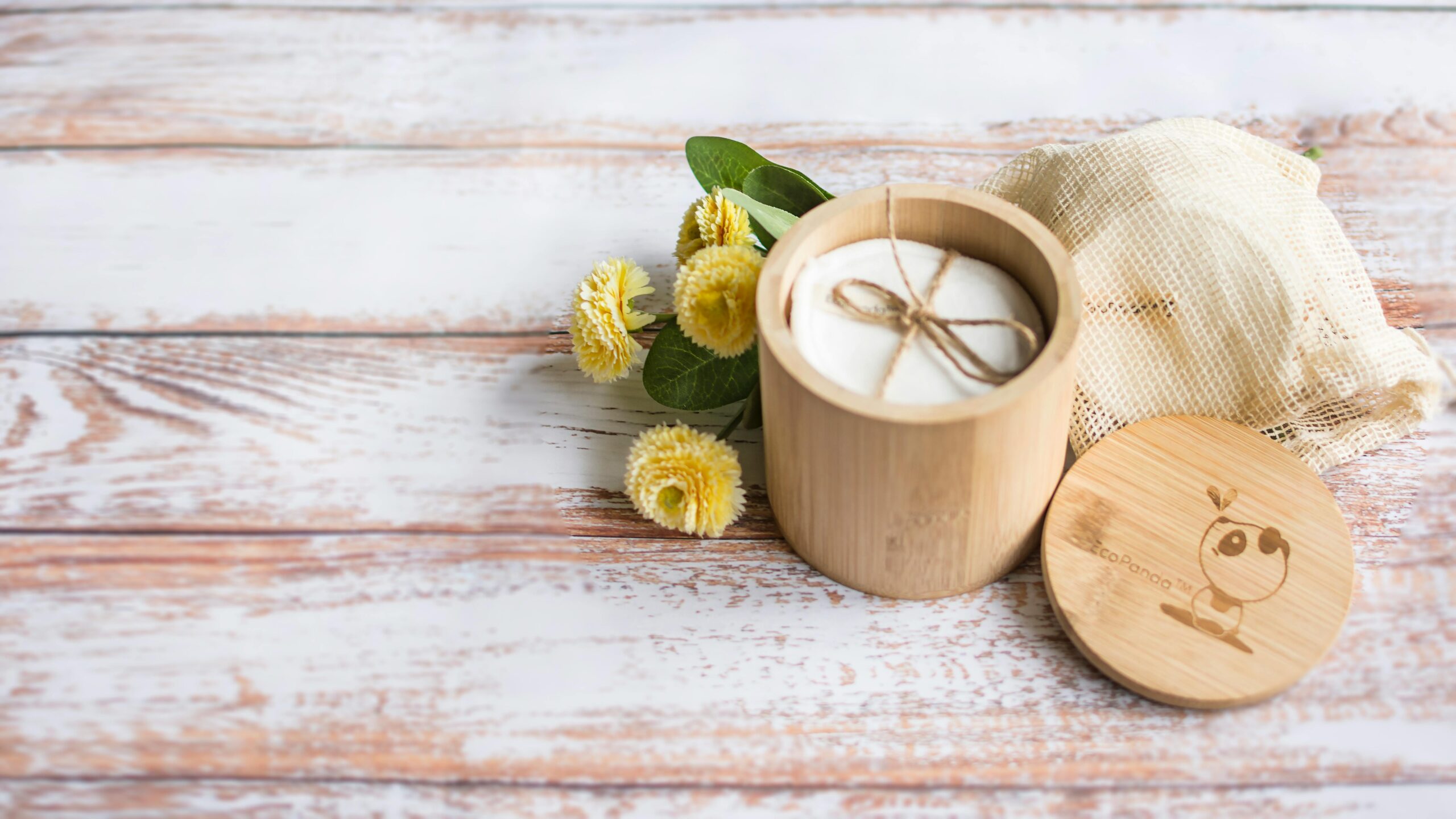 Reusable cotton pads in a bamboo container with flowers, promoting zero waste.