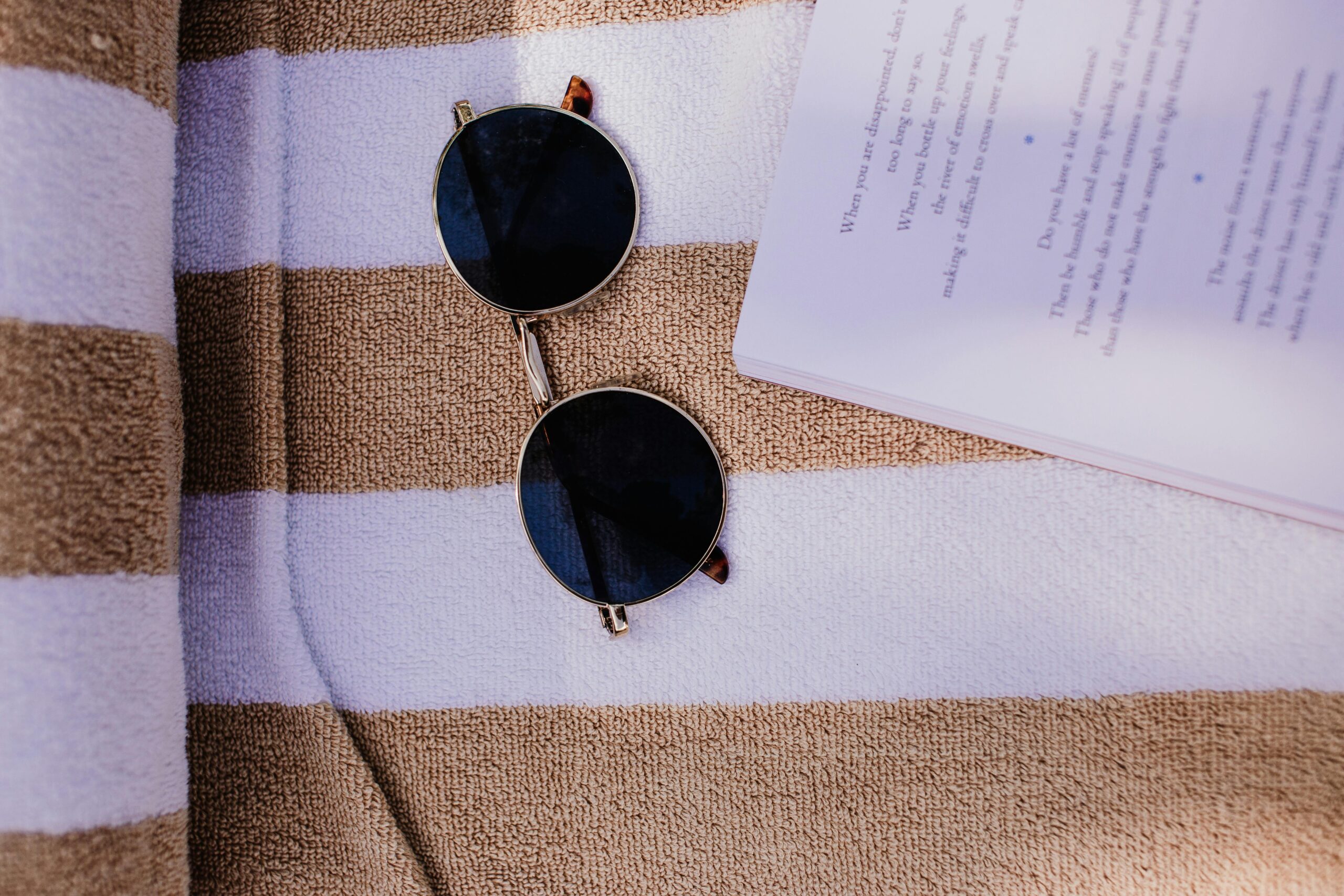 Round sunglasses lying on a striped beach towel with an open book, capturing a summer vibe.