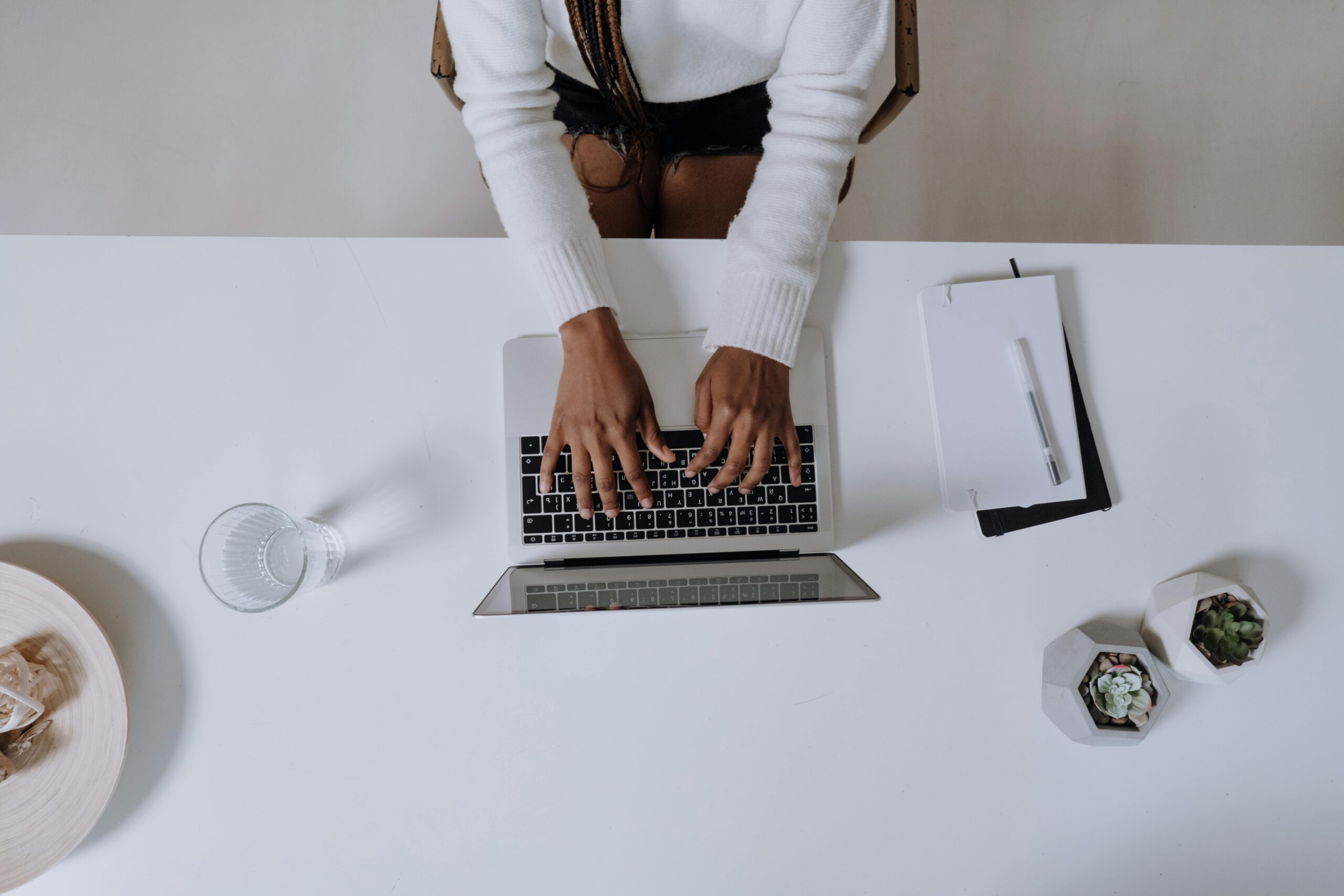 Top view of a woman typing on a laptop at a modern, minimalist home office desk with plants.