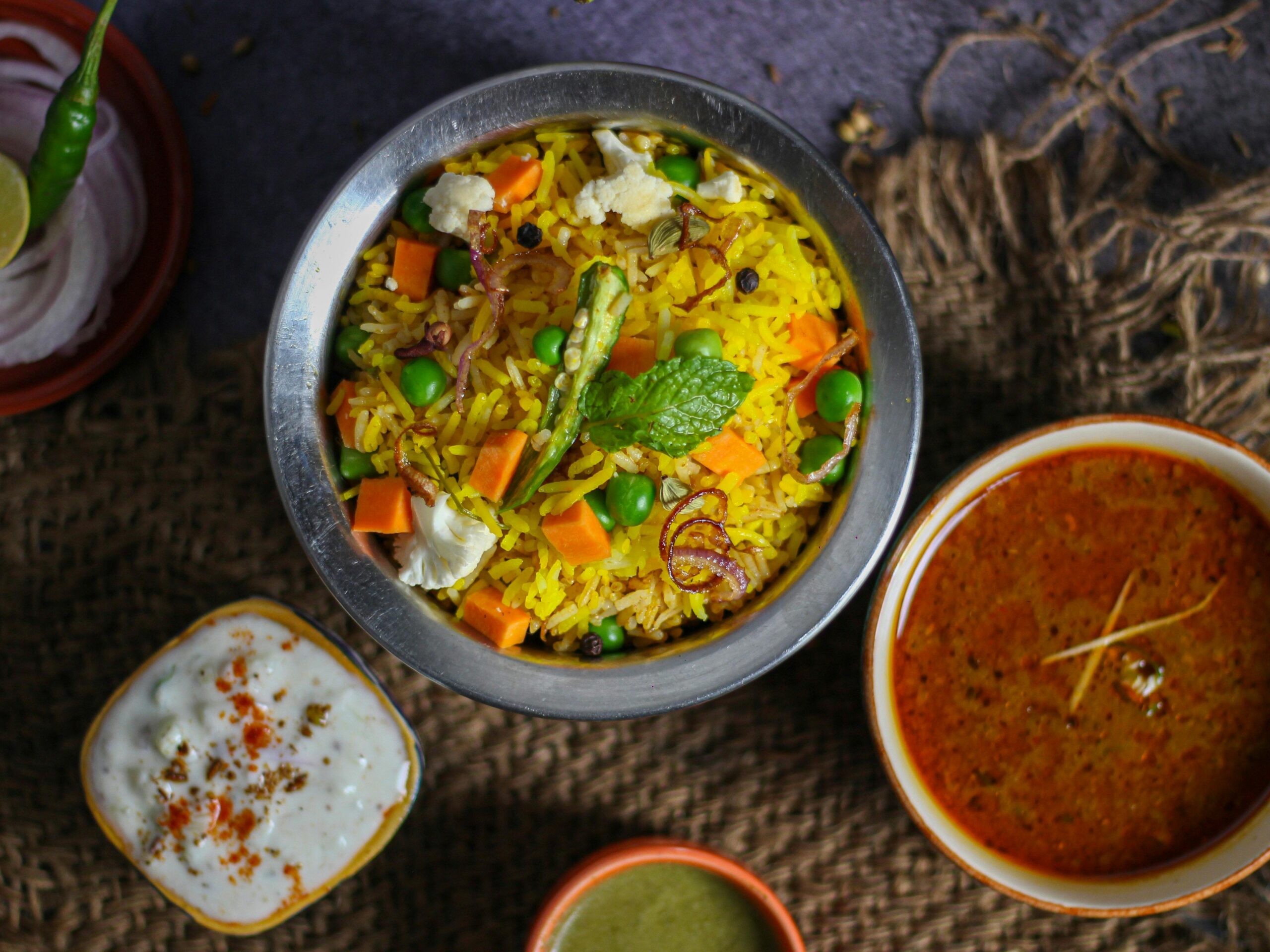 Top view of vibrant Indian biryani with curry and raita on a rustic setting. Perfect for food lovers.