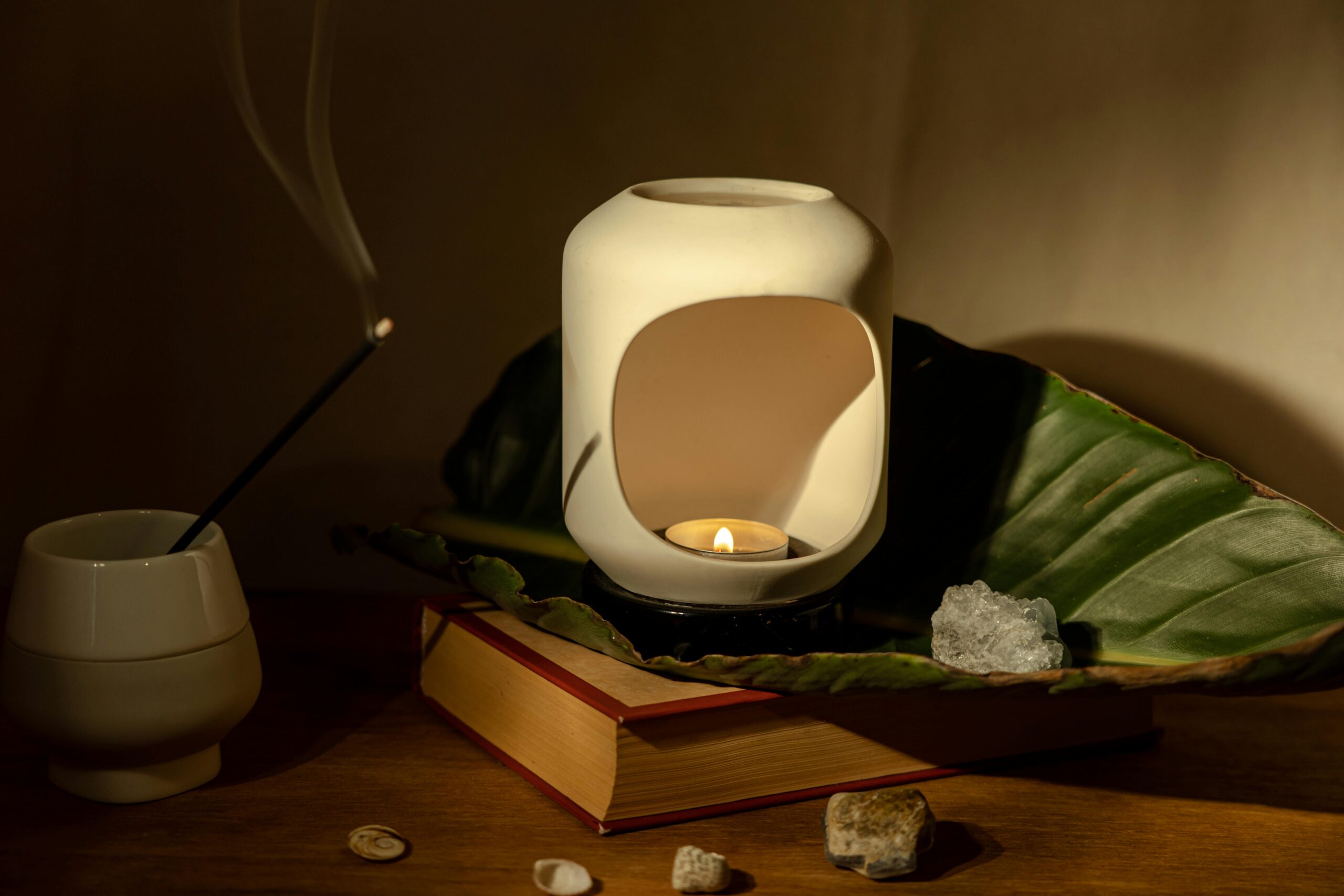 Tranquil aromatherapy scene with candle holder, incense, book, and natural elements for relaxation.