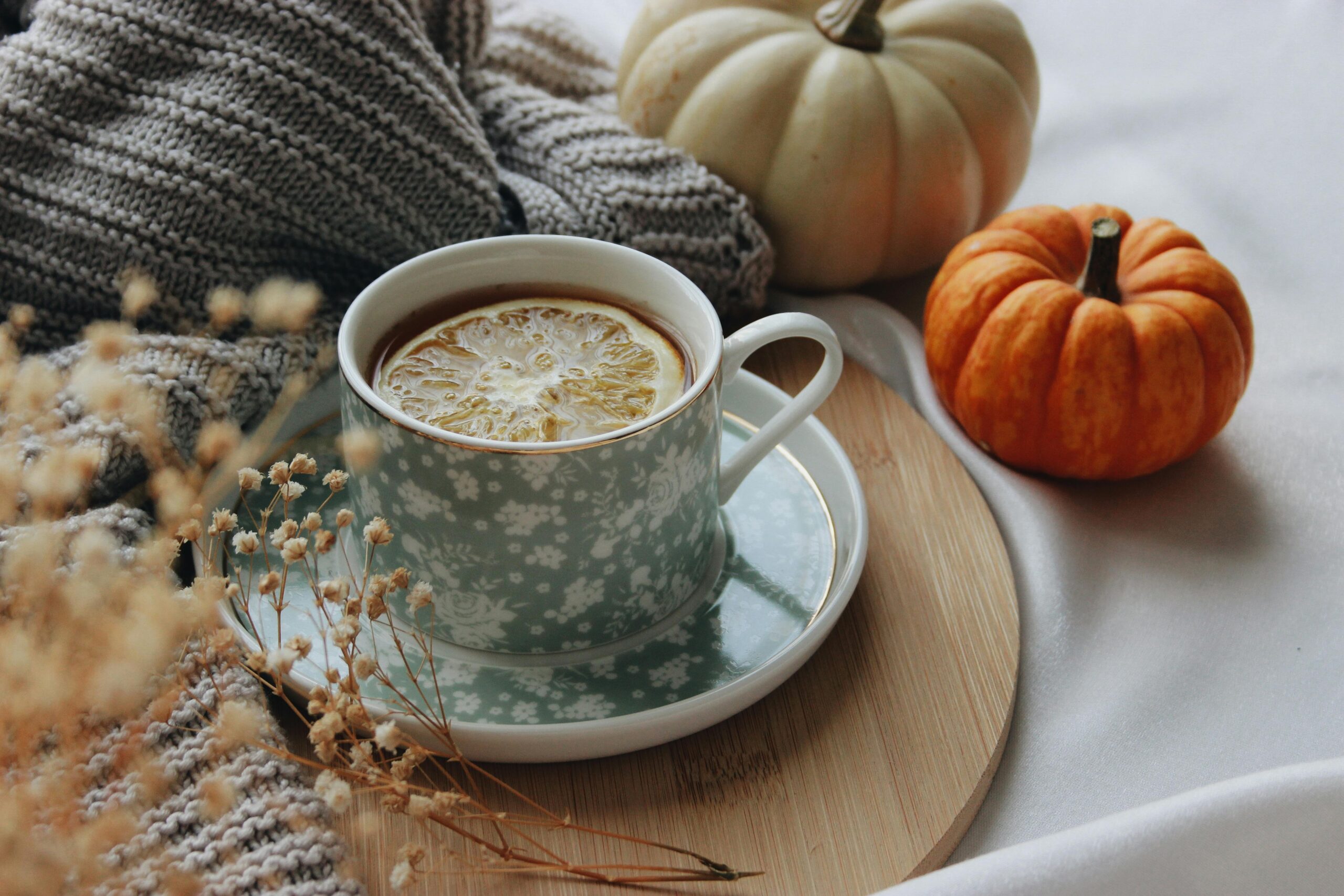 Warm autumn scene with a tea cup, pumpkins, and lemon slice for a cozy seasonal mood.