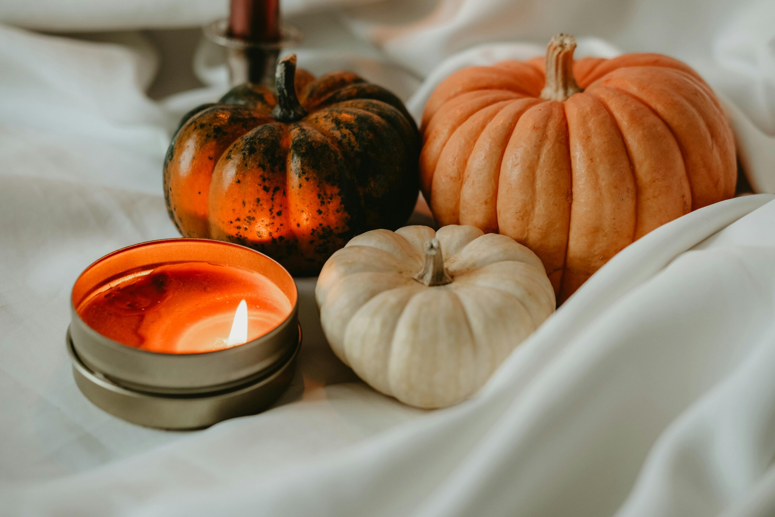 Warm autumn setup with pumpkins and candlelight on a white draped background, perfect for seasonal ambiance.