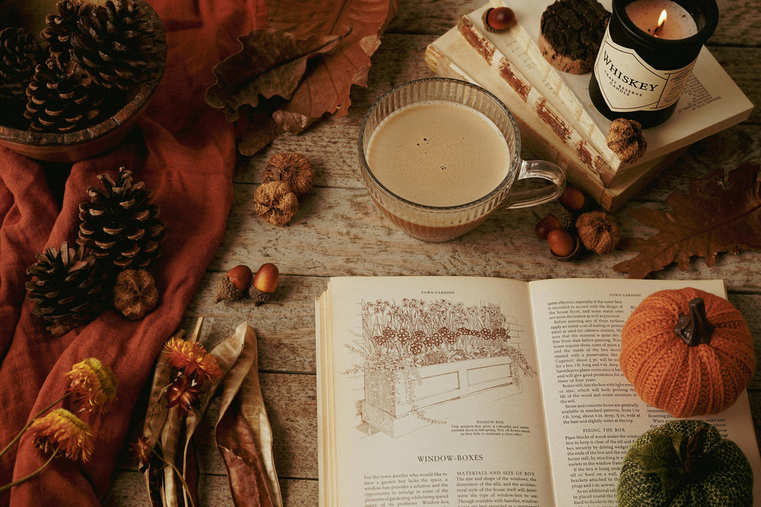 Warm autumn still life with coffee, candles, books, and seasonal decor.