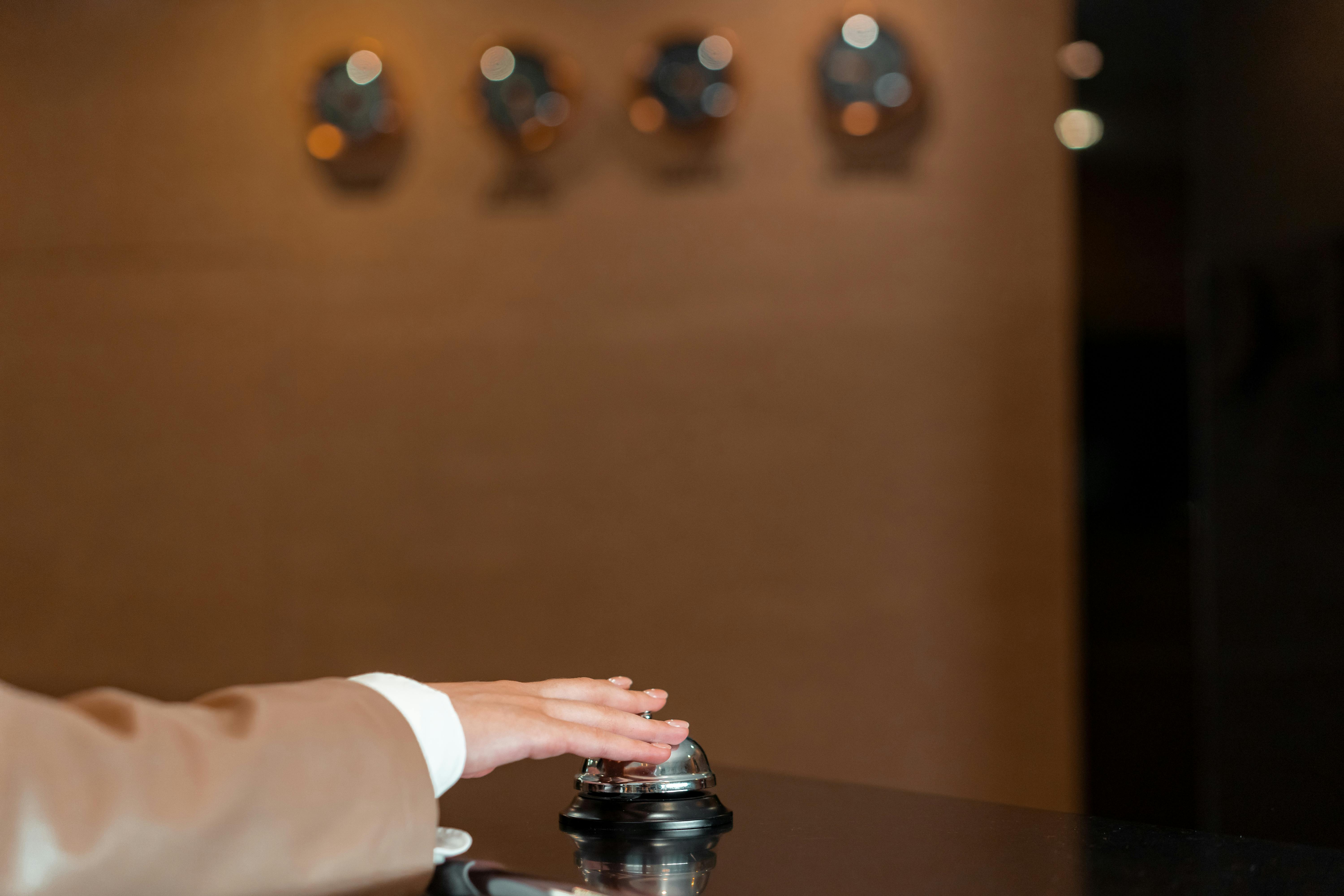 A hand pressing a bell at a hotel reception, symbolizing service and hospitality. Регистрация гостей в гостинице и оформление персональных данных.